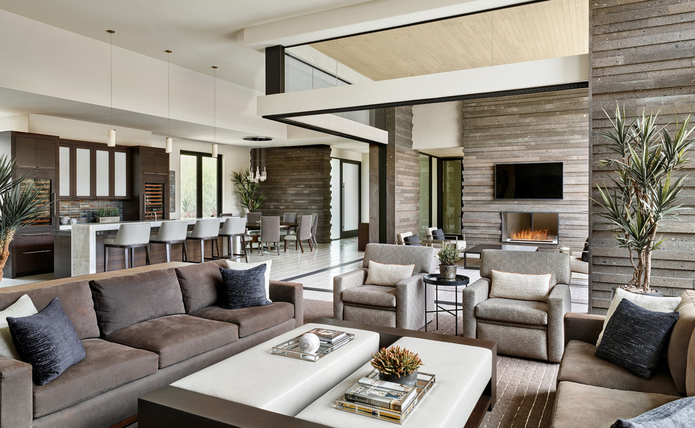 Пример оригинального дизайна: большая открытая гостиная комната в современном стиле с домашним баром, коричневыми стенами, двусторонним камином, фасадом камина из камня, телевизором на стене и белым полом
