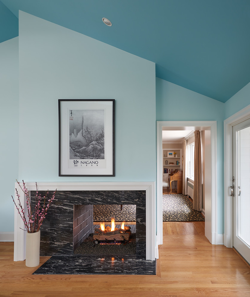 Modelo de sala de estar clásica renovada con paredes azules, suelo de madera en tonos medios, chimenea de doble cara y marco de chimenea de piedra
