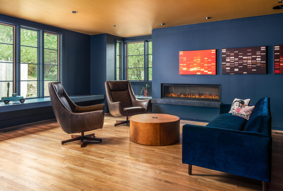Idee per un soggiorno minimal con pareti blu, pavimento in legno massello medio, camino lineare Ribbon e pavimento marrone
