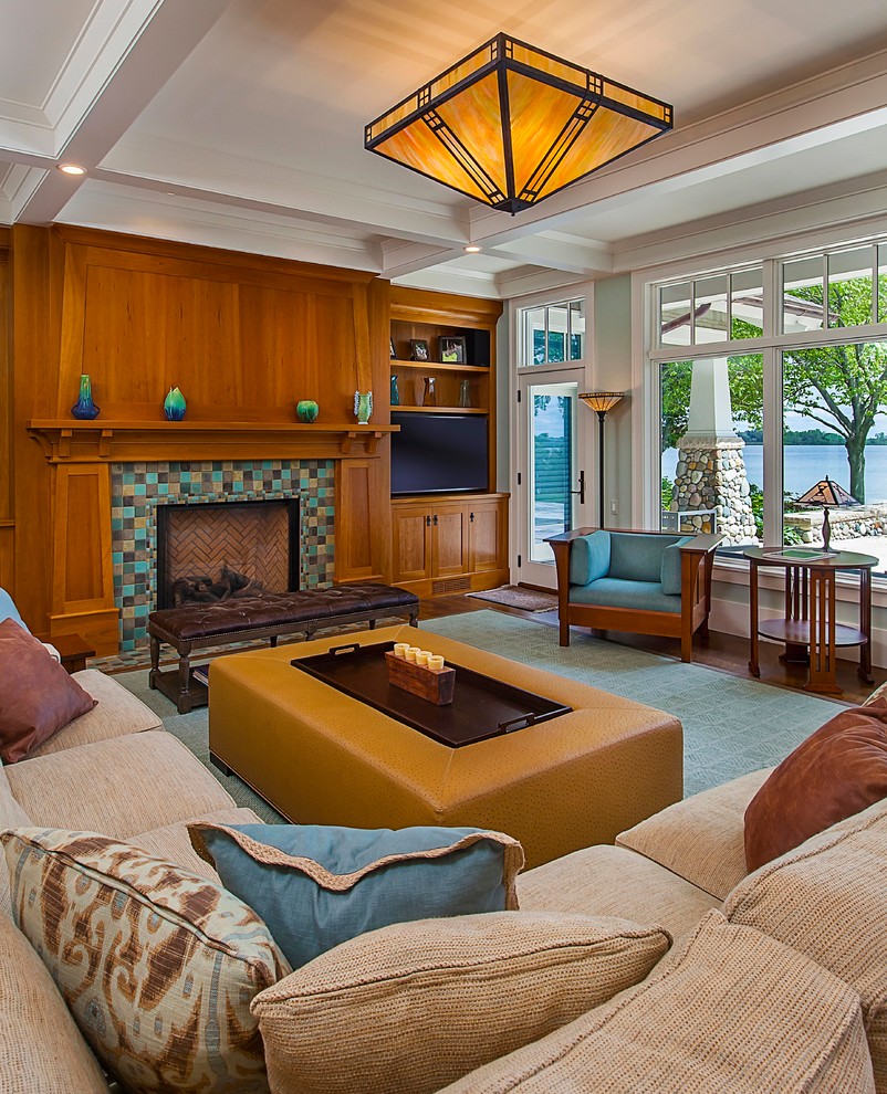 Cette photo montre une grande salle de séjour craftsman avec un sol en bois brun, une cheminée standard, un téléviseur encastré et un manteau de cheminée en carrelage.