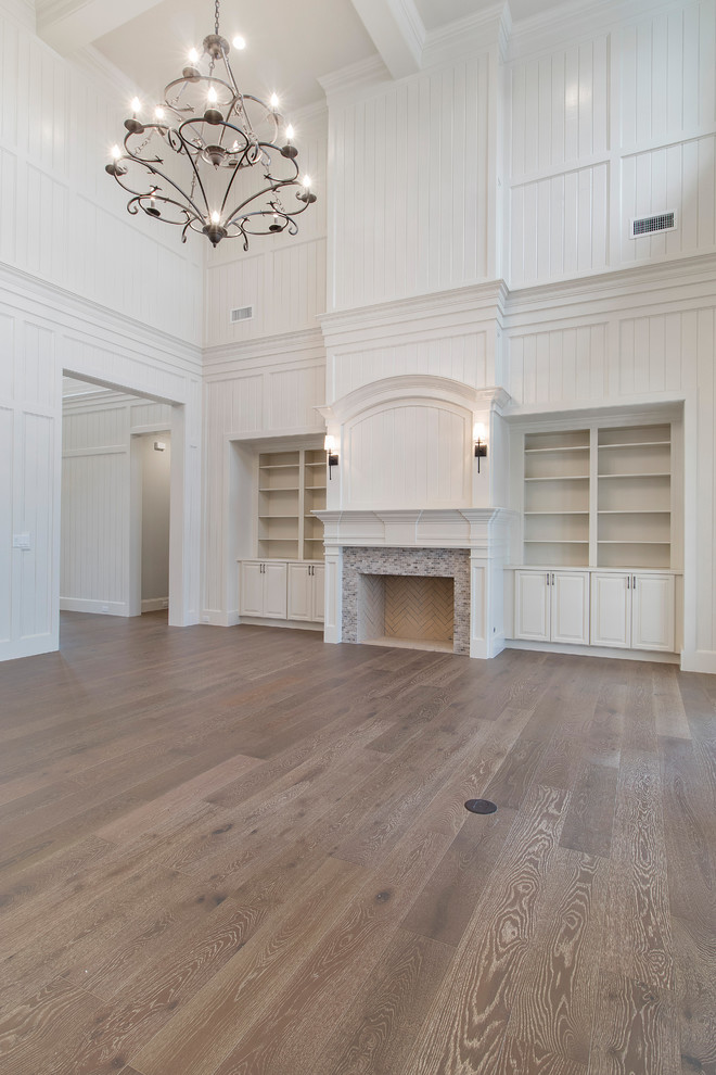 Imagen de sala de estar con biblioteca abierta extra grande con paredes blancas, suelo de madera clara, todas las chimeneas, marco de chimenea de piedra y suelo marrón