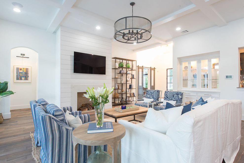 Example of a large beach style open concept medium tone wood floor and brown floor family room design in Houston with white walls, a standard fireplace, a wood fireplace surround and a wall-mounted tv