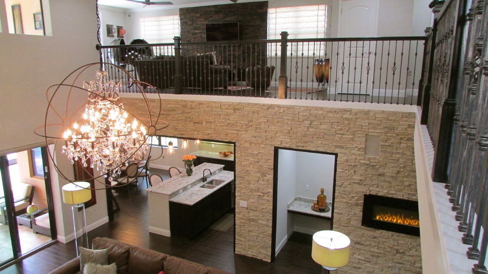 Modelo de sala de estar abierta contemporánea de tamaño medio con paredes beige, suelo de madera oscura, chimenea lineal, televisor colgado en la pared y marco de chimenea de piedra
