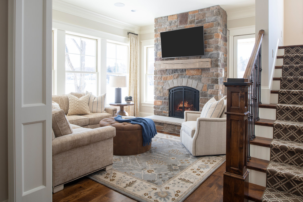 Inspiration for a traditional open plan games room in Minneapolis with beige walls, dark hardwood flooring, a standard fireplace, a stone fireplace surround, a wall mounted tv and brown floors.