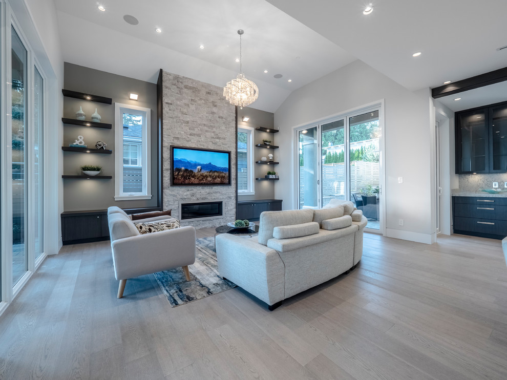 Offenes, Großes Modernes Wohnzimmer mit grauer Wandfarbe, hellem Holzboden, Gaskamin, Kaminumrandung aus Stein, TV-Wand und grauem Boden in Vancouver