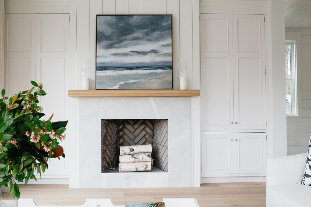 Imagen de sala de estar abierta costera de tamaño medio con paredes blancas, suelo de madera clara, todas las chimeneas y marco de chimenea de piedra