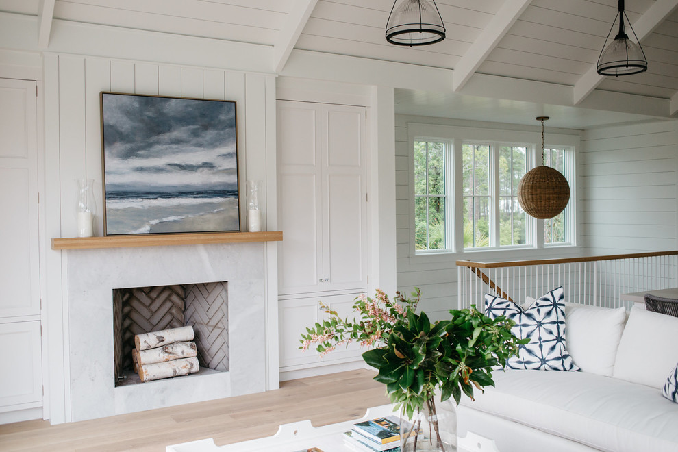 Imagen de sala de estar abierta costera de tamaño medio con paredes blancas, suelo de madera clara, todas las chimeneas y marco de chimenea de piedra