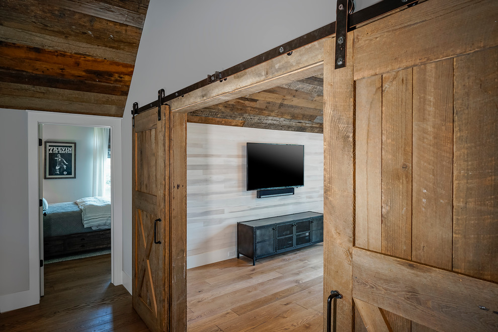 Lantlig inredning av ett stort allrum, med ett spelrum, ljust trägolv, en väggmonterad TV och brunt golv
