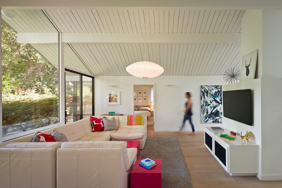 Пример оригинального дизайна: гостиная комната в стиле ретро с белыми стенами, телевизором на стене, светлым паркетным полом и ковром на полу