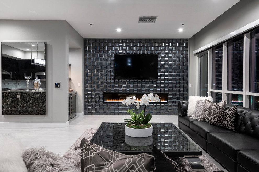 На фото: большая открытая гостиная комната в современном стиле с домашним баром, серыми стенами, полом из керамической плитки, стандартным камином, фасадом камина из плитки, телевизором на стене и серым полом