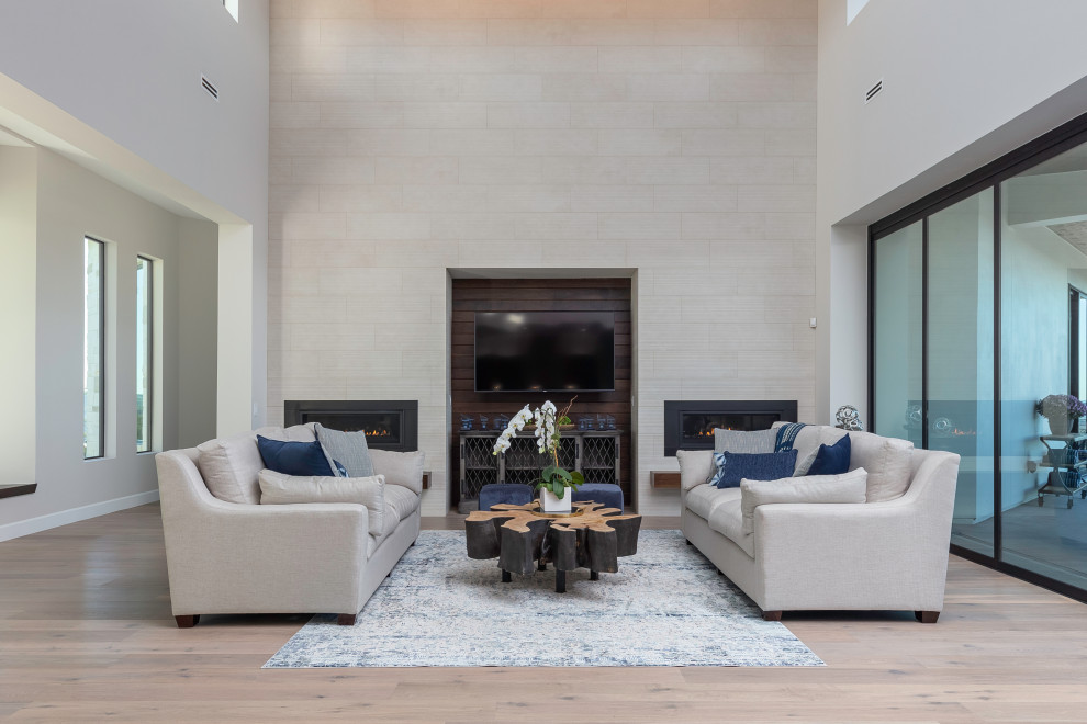 Modelo de sala de estar abierta clásica renovada con paredes blancas, suelo de madera clara, marco de chimenea de baldosas y/o azulejos y suelo beige