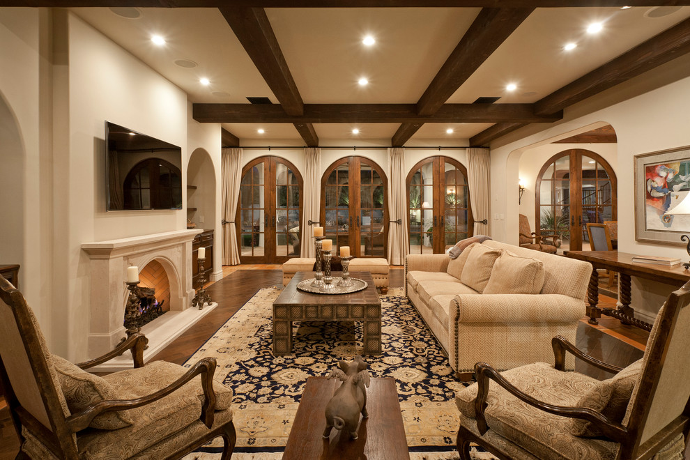 Mediterranes Wohnzimmer mit beiger Wandfarbe, dunklem Holzboden, Kamin, Kaminumrandung aus Stein und TV-Wand in Phoenix