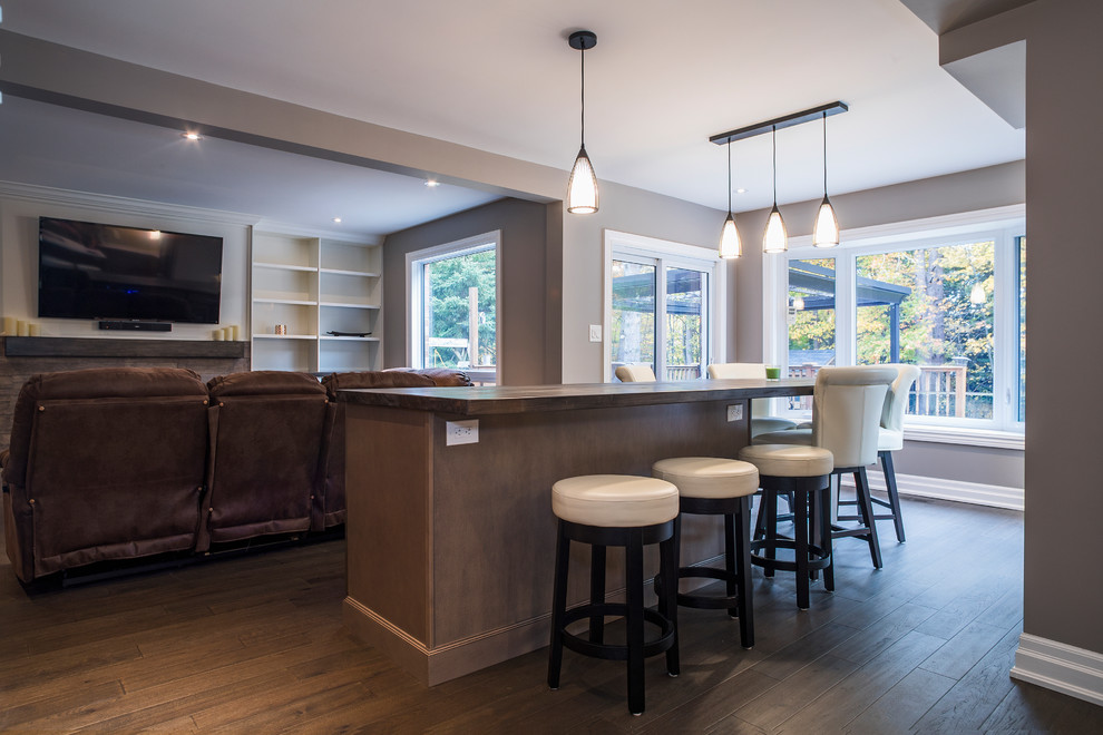 Photo of a large contemporary open plan games room in Toronto with a home bar, grey walls, medium hardwood flooring, a standard fireplace, a brick fireplace surround, a wall mounted tv and brown floors.