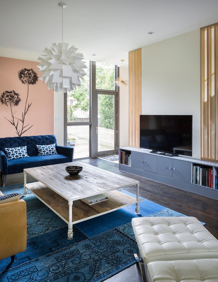 Пример оригинального дизайна: большая открытая гостиная комната в скандинавском стиле с с книжными шкафами и полками, разноцветными стенами, темным паркетным полом, отдельно стоящим телевизором, коричневым полом и синим диваном без камина