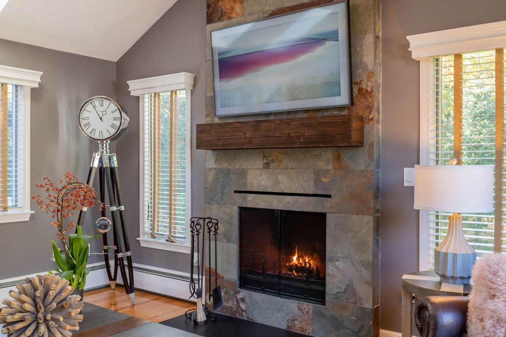 Imagen de sala de estar contemporánea de tamaño medio con paredes grises, suelo de madera en tonos medios, todas las chimeneas, marco de chimenea de piedra, televisor colgado en la pared y suelo marrón