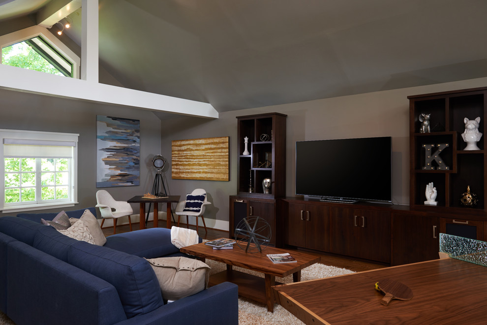 На фото: большая открытая комната для игр в стиле ретро с серыми стенами, паркетным полом среднего тона, отдельно стоящим телевизором и коричневым полом без камина
