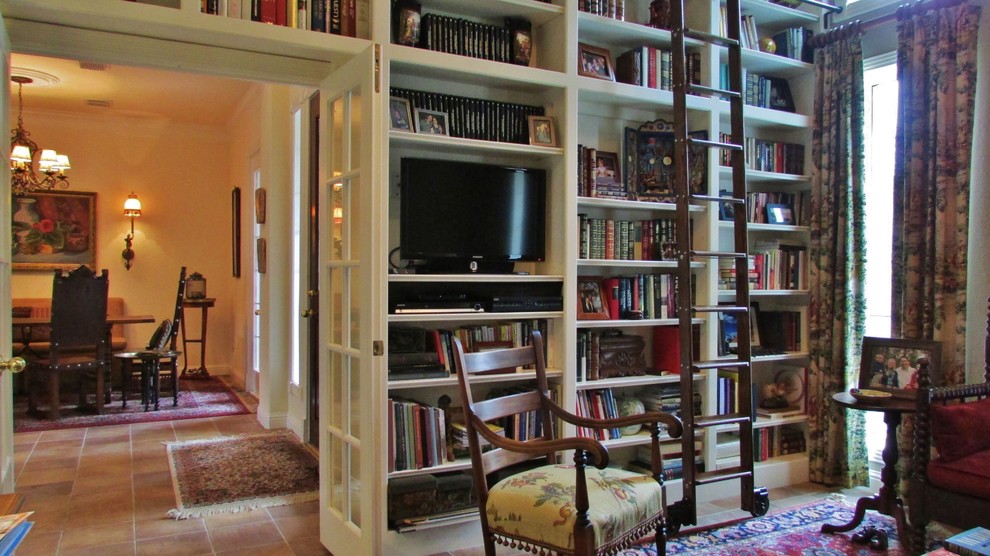 Cette photo montre une salle de séjour chic de taille moyenne et fermée avec une bibliothèque ou un coin lecture, un mur beige, tomettes au sol, aucune cheminée et un téléviseur indépendant.