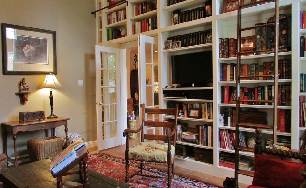 Idée de décoration pour une salle de séjour tradition de taille moyenne et fermée avec une bibliothèque ou un coin lecture, un mur beige, tomettes au sol, aucune cheminée et un téléviseur indépendant.