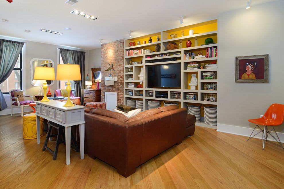 Ejemplo de sala de estar con biblioteca ecléctica sin chimenea con paredes grises, suelo de madera en tonos medios y pared multimedia