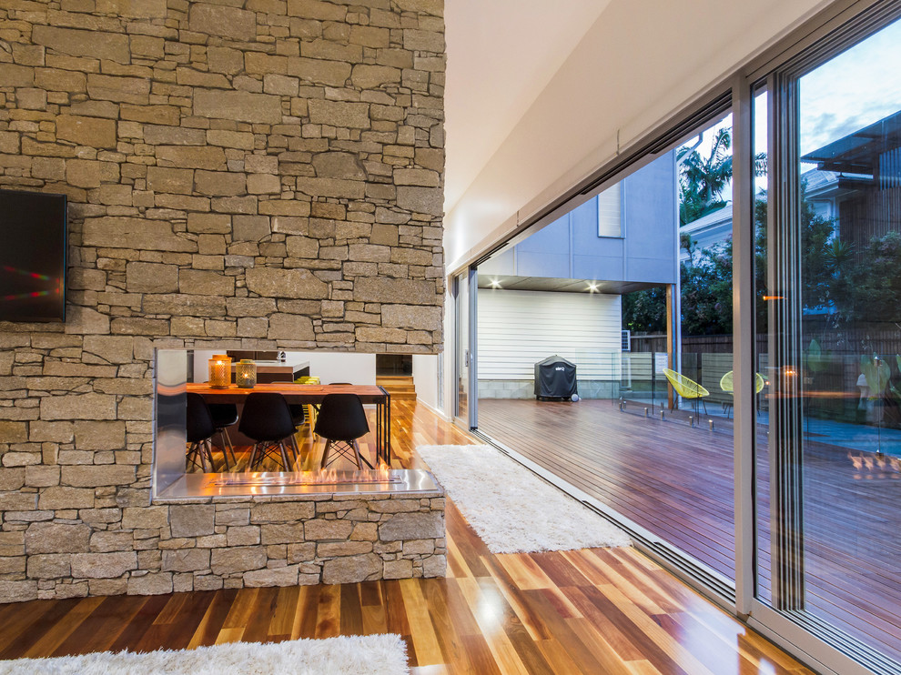 Family room - mid-sized contemporary open concept medium tone wood floor family room idea in Brisbane with white walls, a two-sided fireplace, a stone fireplace and a wall-mounted tv