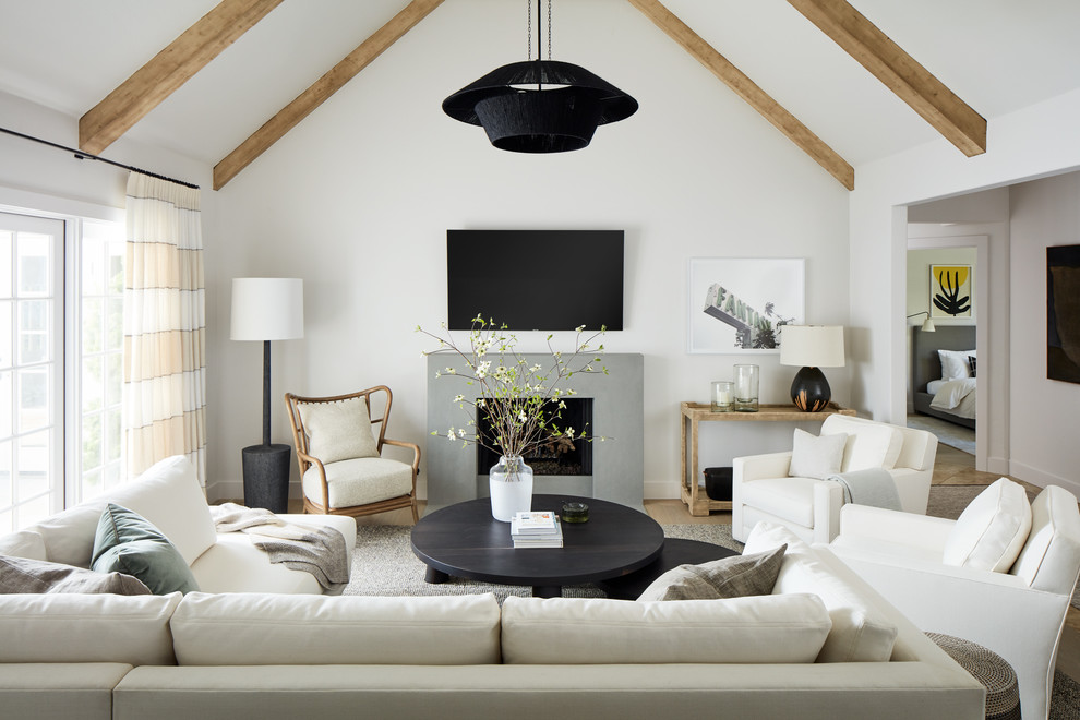 Imagen de sala de estar abierta costera de tamaño medio con paredes blancas, todas las chimeneas, televisor colgado en la pared, suelo de madera clara, marco de chimenea de hormigón y alfombra
