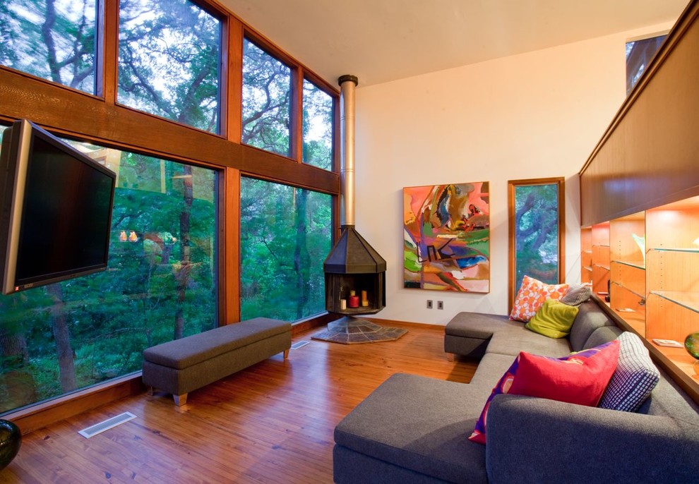 Idée de décoration pour une salle de séjour design avec un mur beige, un sol en bois brun, une cheminée d'angle et un téléviseur d'angle.