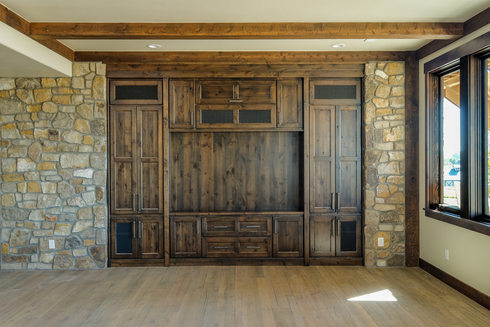 Diseño de sala de estar cerrada rústica grande con paredes beige, suelo de madera clara y pared multimedia