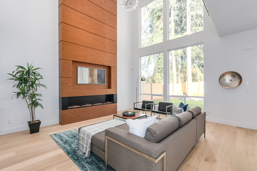 Cette image montre une salle de séjour design avec un mur blanc, parquet clair, une cheminée ribbon, un manteau de cheminée en bois et un téléviseur fixé au mur.