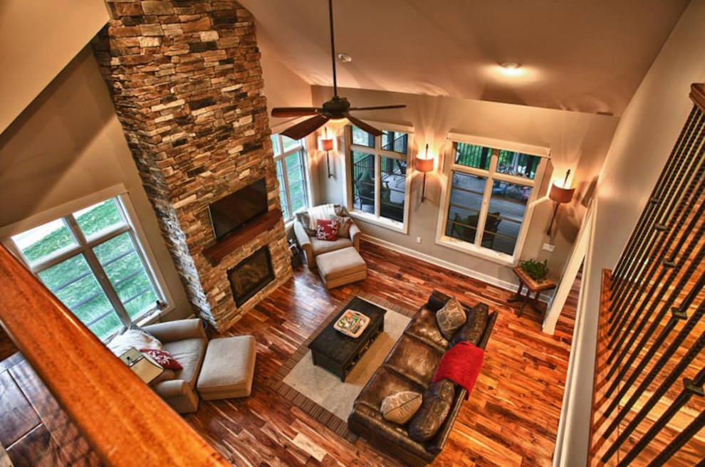 Aménagement d'une salle de séjour craftsman ouverte avec un mur beige, un sol en bois brun, une cheminée standard, un manteau de cheminée en pierre et un téléviseur fixé au mur.