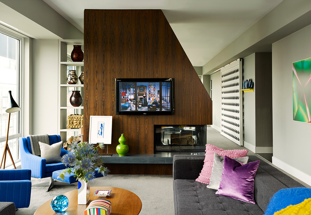 Modelo de sala de estar abierta actual grande con paredes grises, moqueta, chimenea de doble cara, marco de chimenea de madera y televisor colgado en la pared