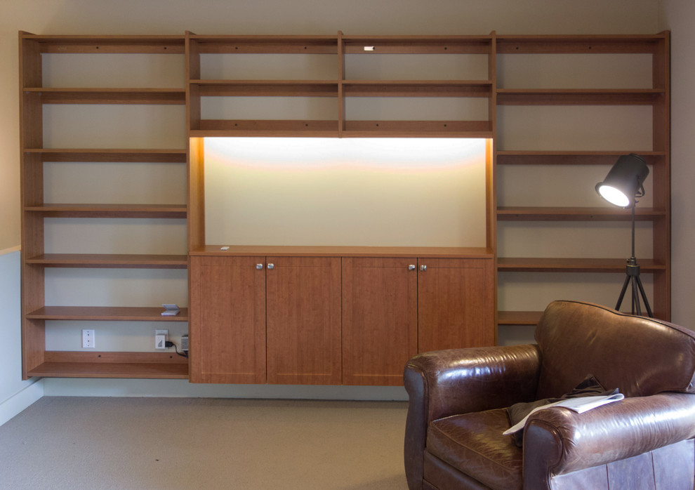 Bild på ett funkis allrum med öppen planlösning, med ett bibliotek, vita väggar, heltäckningsmatta, en spiselkrans i metall och en väggmonterad TV