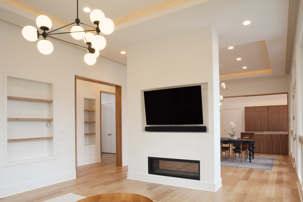 Example of a large trendy open concept light wood floor and brown floor family room design in New York with white walls, a two-sided fireplace, a plaster fireplace and a media wall
