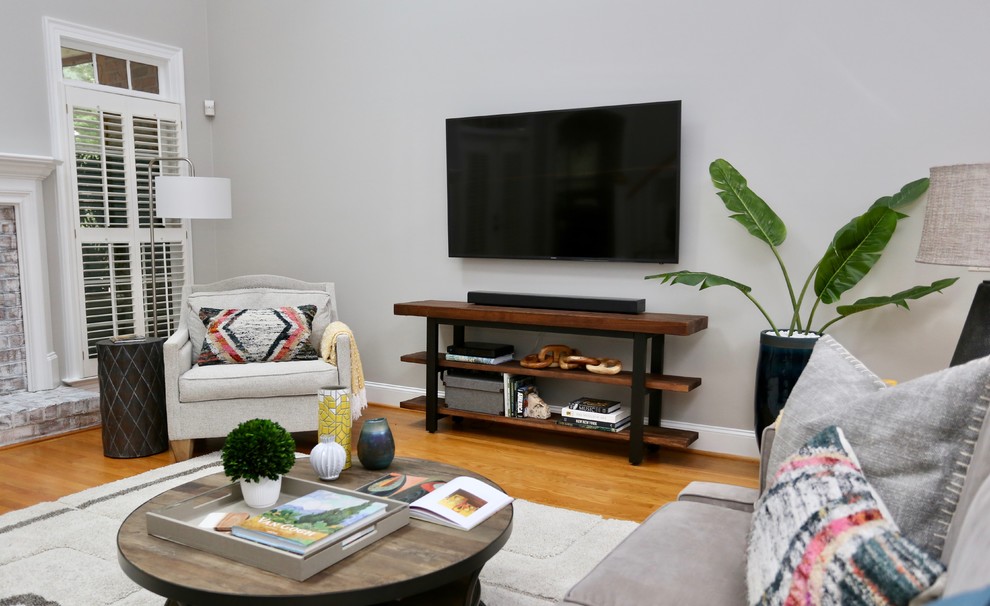 Imagen de sala de estar abierta bohemia grande con paredes grises, suelo de madera en tonos medios y televisor colgado en la pared