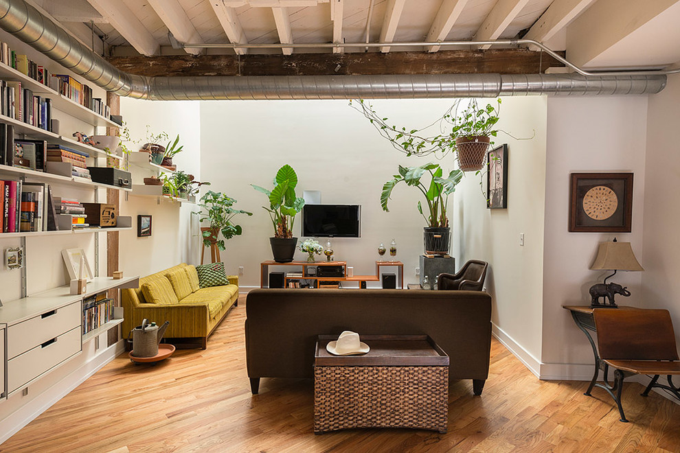 Aménagement d'une salle de séjour industrielle ouverte avec un mur blanc, un sol en bois brun et un téléviseur fixé au mur.