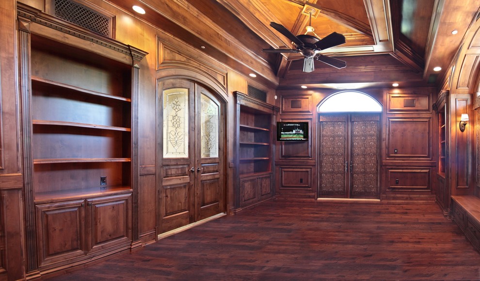 Foto de sala de estar con biblioteca cerrada clásica grande sin chimenea con paredes marrones, suelo de madera en tonos medios y televisor colgado en la pared