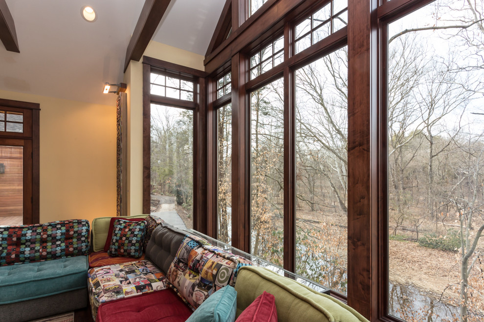 Modelo de sala de estar abierta rural grande con paredes beige, suelo de madera oscura, chimenea de doble cara, marco de chimenea de piedra y televisor colgado en la pared