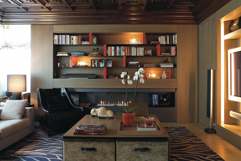 Foto de sala de estar con biblioteca abierta bohemia de tamaño medio con paredes marrones, suelo de madera en tonos medios, chimenea lineal, marco de chimenea de metal y pared multimedia