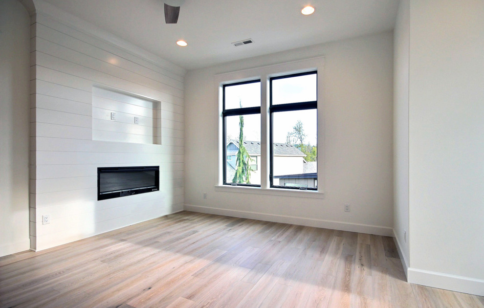 На фото: огромная двухуровневая гостиная комната в стиле кантри с белыми стенами, светлым паркетным полом, горизонтальным камином, фасадом камина из вагонки, телевизором на стене и коричневым полом с