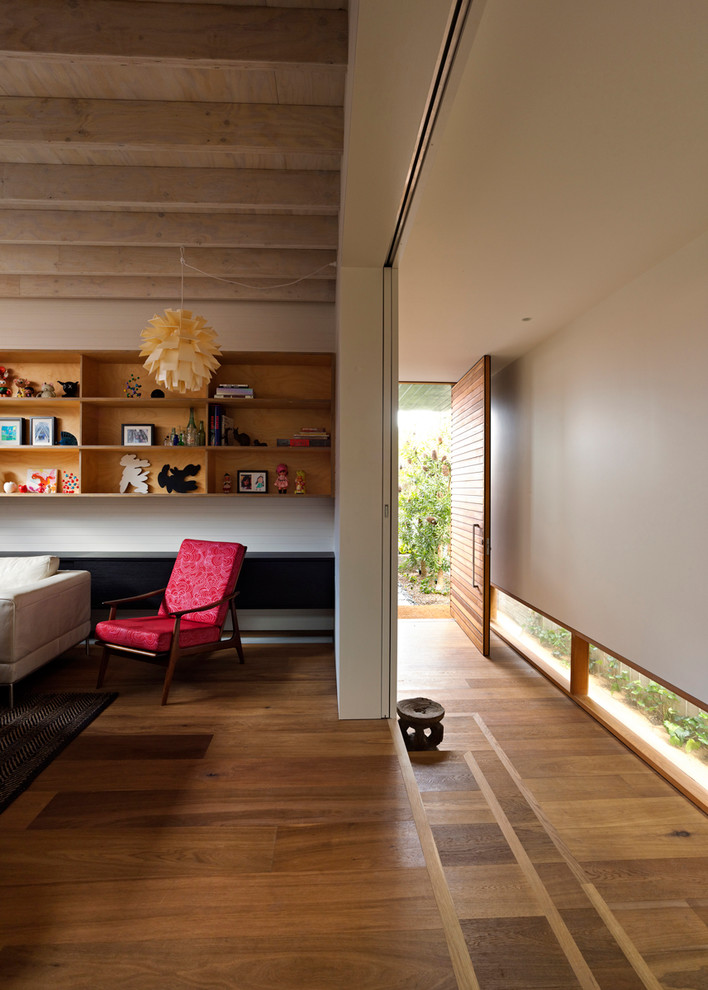Cette image montre une salle de séjour design de taille moyenne et ouverte avec une bibliothèque ou un coin lecture, un mur blanc, un sol en bois brun et aucun téléviseur.