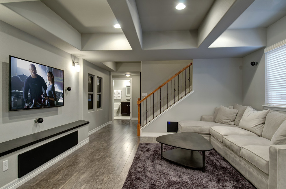Modelo de sala de estar con barra de bar abierta contemporánea grande con paredes grises, suelo de madera oscura, todas las chimeneas, marco de chimenea de piedra, televisor colgado en la pared y suelo marrón