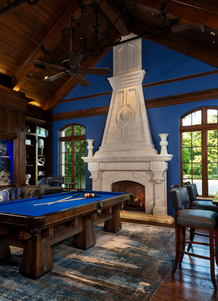 マイアミにあるトランジショナルスタイルのおしゃれなファミリールーム (ゲームルーム、青い壁、無垢フローリング、標準型暖炉、石材の暖炉まわり、茶色い床) の写真
