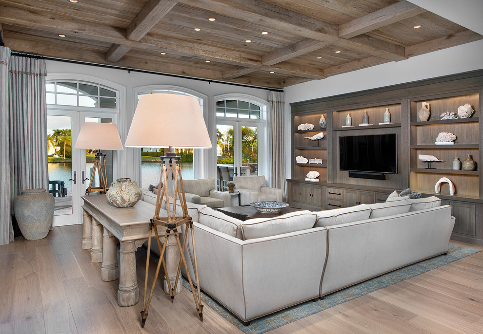 Imagen de sala de estar costera con paredes blancas, suelo de madera clara y pared multimedia