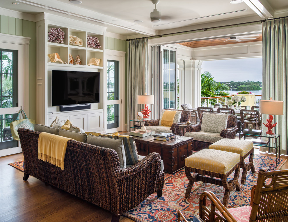 Modelo de sala de estar tropical grande con paredes verdes, suelo de madera en tonos medios y pared multimedia