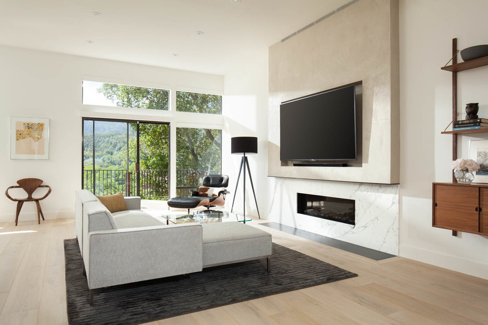 Bild på ett funkis allrum med öppen planlösning, med vita väggar, ljust trägolv, en bred öppen spis, en spiselkrans i sten och en väggmonterad TV