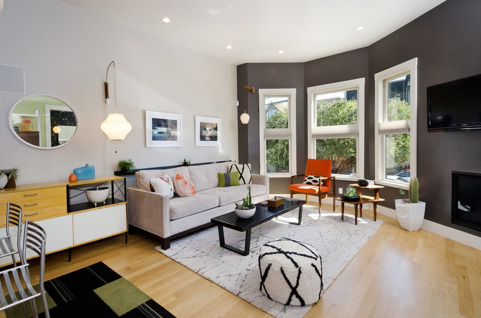 Immagine di un soggiorno design aperto con parquet chiaro, camino classico, TV a parete e pareti grigie