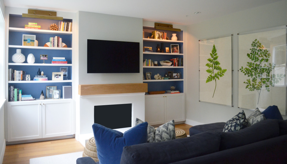 Modelo de sala de estar actual de tamaño medio con paredes blancas, suelo de madera en tonos medios, todas las chimeneas, marco de chimenea de yeso y televisor colgado en la pared