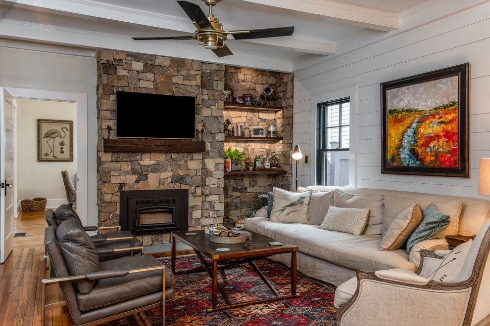 Foto de sala de estar cerrada marinera con paredes grises, suelo de madera en tonos medios, marco de chimenea de piedra y televisor colgado en la pared