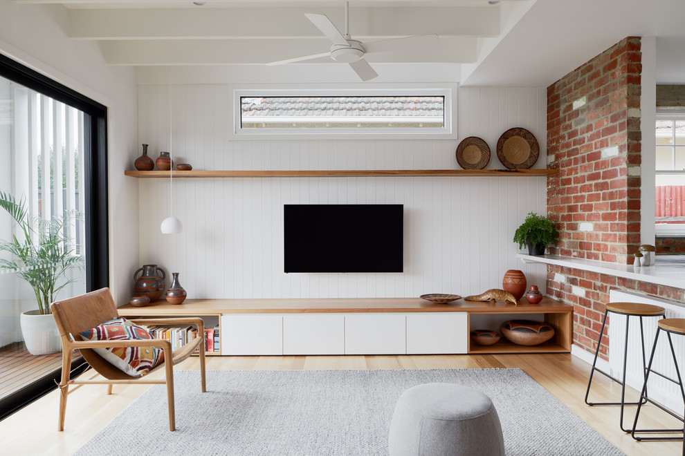 Modelo de sala de estar abierta actual sin chimenea con paredes blancas, suelo de madera clara y televisor colgado en la pared