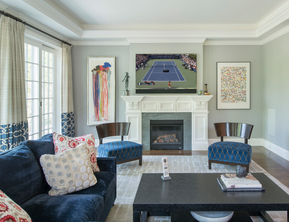 This is an example of a large contemporary open plan games room in Boston with dark hardwood flooring, a standard fireplace, a wooden fireplace surround, a wall mounted tv, grey walls and brown floors.