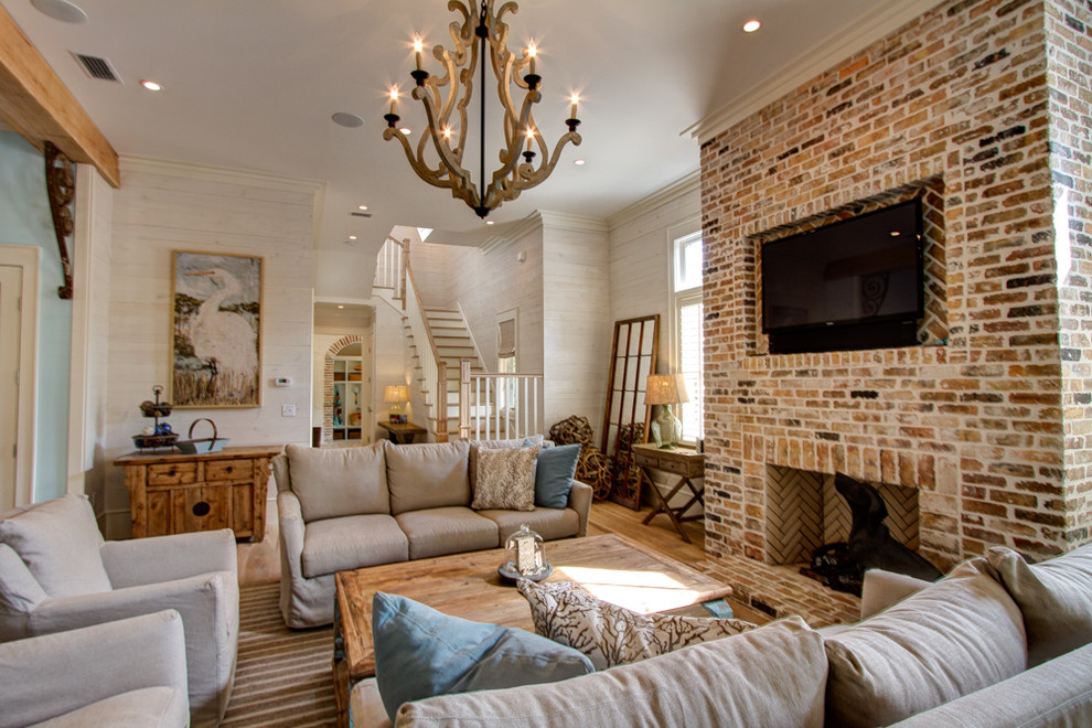 На фото: огромная открытая гостиная комната в морском стиле с белыми стенами, стандартным камином, фасадом камина из кирпича и телевизором на стене